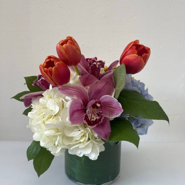 Mixed bouquet with tulips, orchids, and hydrangeas in a glass vase
