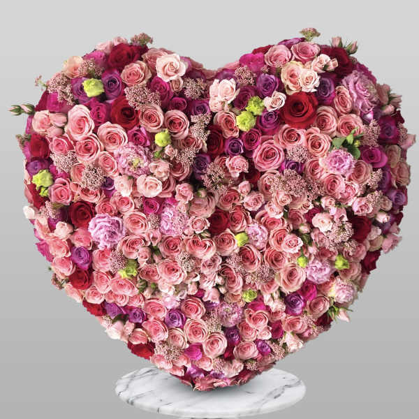 Heart-shaped arrangement of pink and red roses on a marble stand