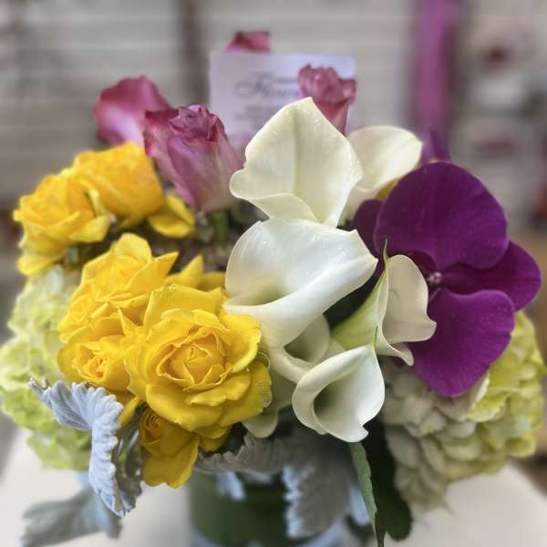 Bouquet of yellow roses, white calla lilies, and purple orchids in a glass vase