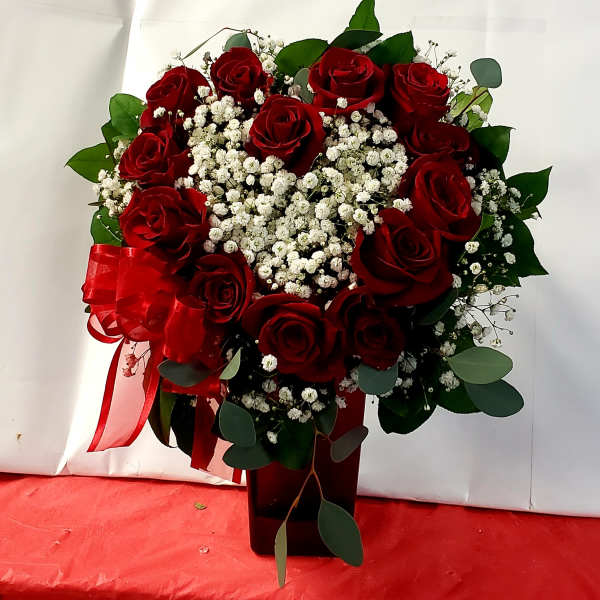 Red roses and white baby's breath in a dark vase with a red ribbon