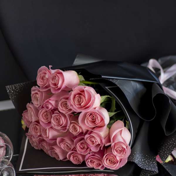 Bouquet of pink roses wrapped in black paper with a pale ribbon