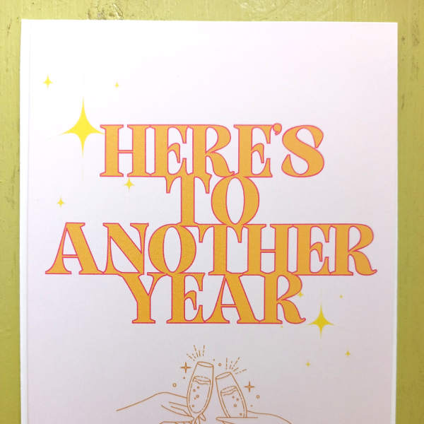 Greeting card with “Here’s to Another Year” text and hands clinking champagne glasses.