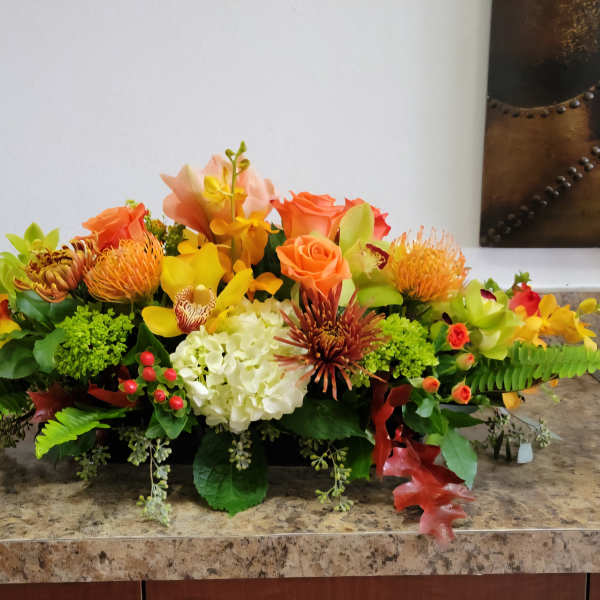 Low floral centerpiece with orange, yellow, and white blooms in a rectangular container