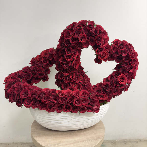 Two intertwined heart shapes made of red roses in a white bowl-shaped vase