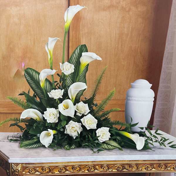 White calla lilies and roses arranged with greenery beside a white urn