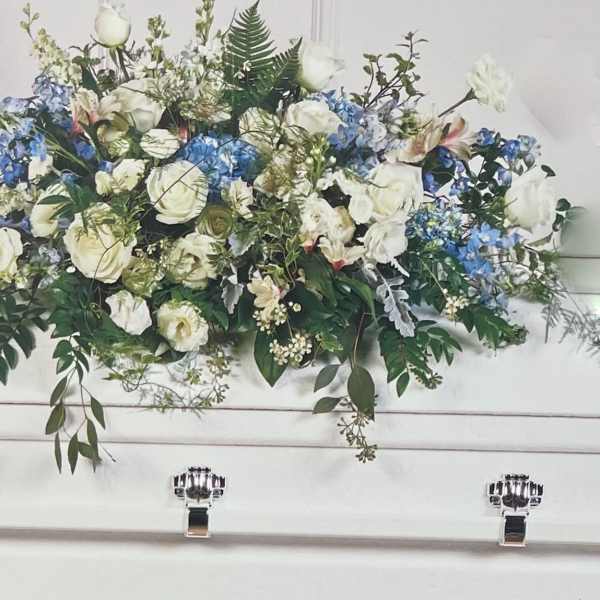 White and blue floral arrangement in a white casket