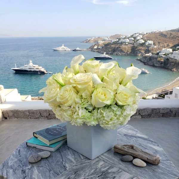 White floral arrangement in a square vase on a table overlooking the sea