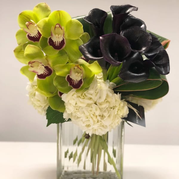 Green orchids, dark calla lilies, and white hydrangeas in a clear glass cube vase