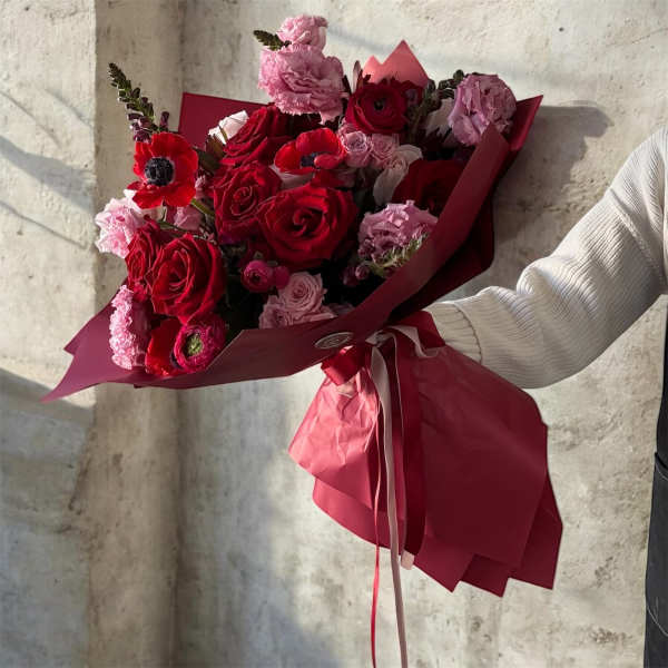 Bouquet of red and pink roses with red anemones wrapped in burgundy paper