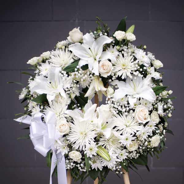 White floral wreath on a wooden easel with a ribbon bow