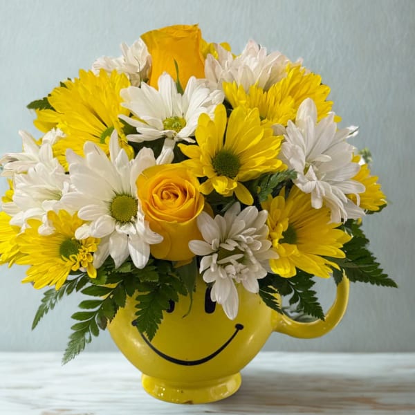 Yellow and white daisy bouquet in a smiley-face mug