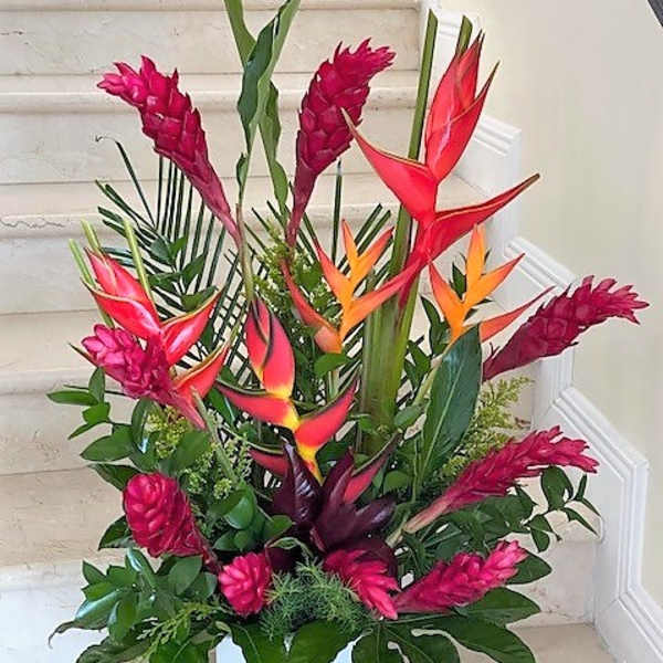 Tall tropical arrangement with red and orange flowers in a white square vase