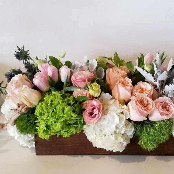 Low floral arrangement in a wooden box with pink and peach roses