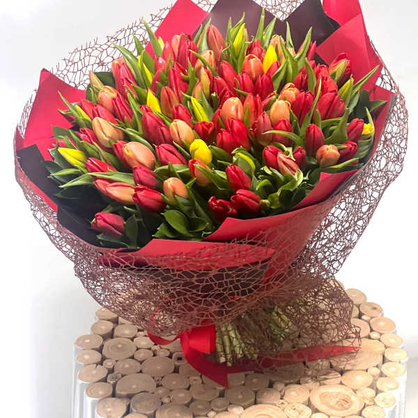 Large bouquet of red, pink, peach, and yellow tulips wrapped in red and black paper