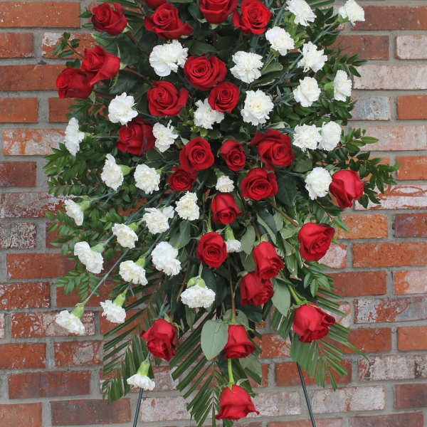 Tall standing spray of red roses and white carnations with palm fronds on an easel