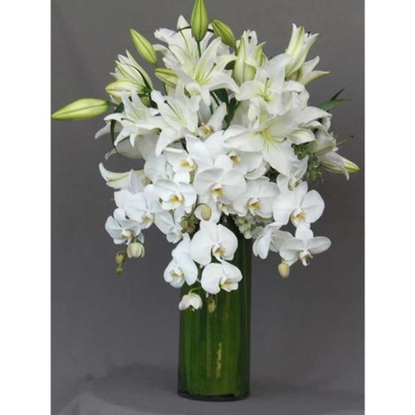 White lilies and orchids arranged in a tall green vase