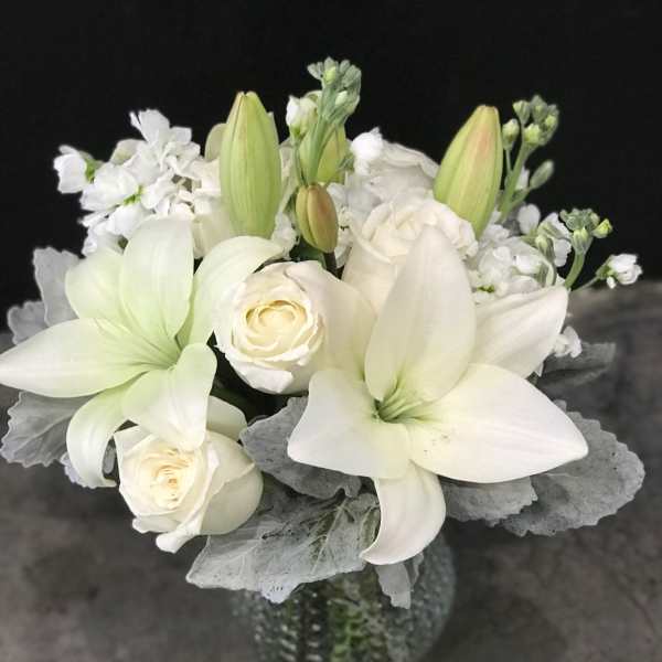 White lilies and roses in a glass vase with silver foliage