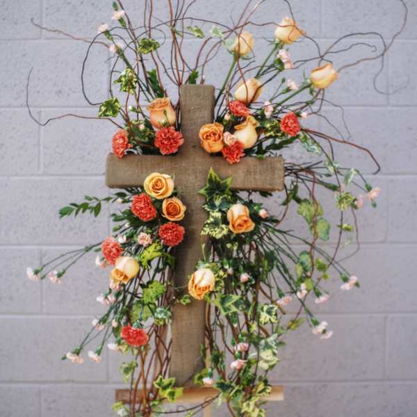 Floral cross arrangement with peach roses and orange carnations
