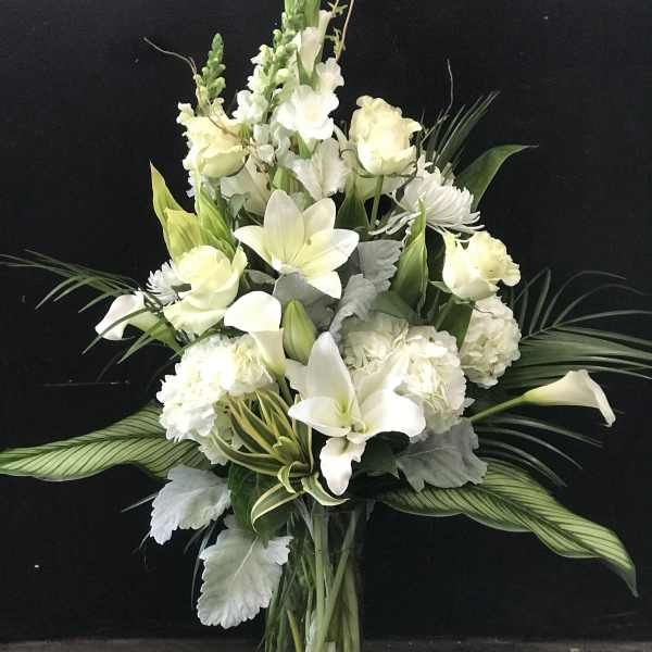 White floral arrangement in a clear glass vase with lilies and calla lilies