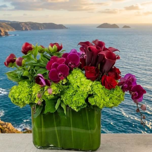 Arrangement of green hydrangeas, orchids, roses, and calla lilies in a glass vase