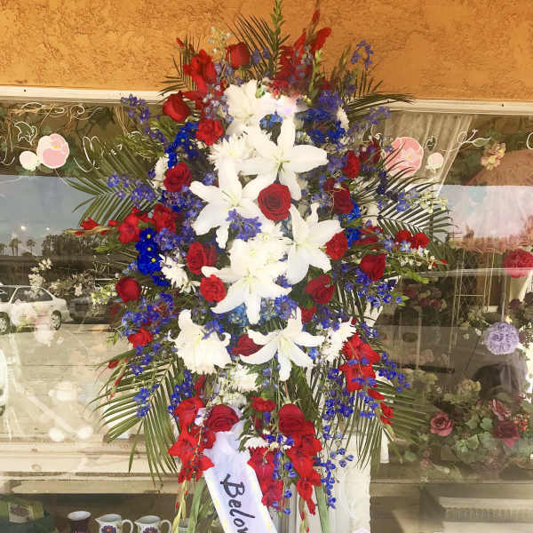 Standing funeral spray with red roses, white lilies, and blue flowers