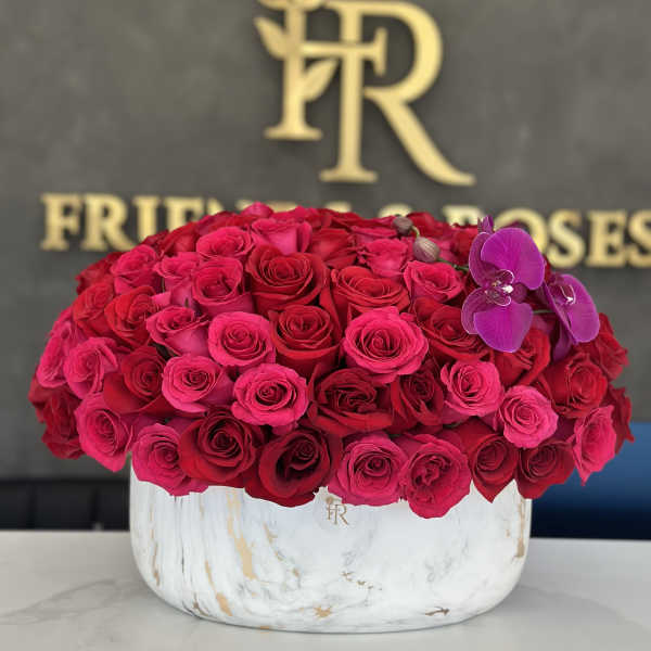 Round arrangement of red and pink roses in a white marble vase with purple orchids