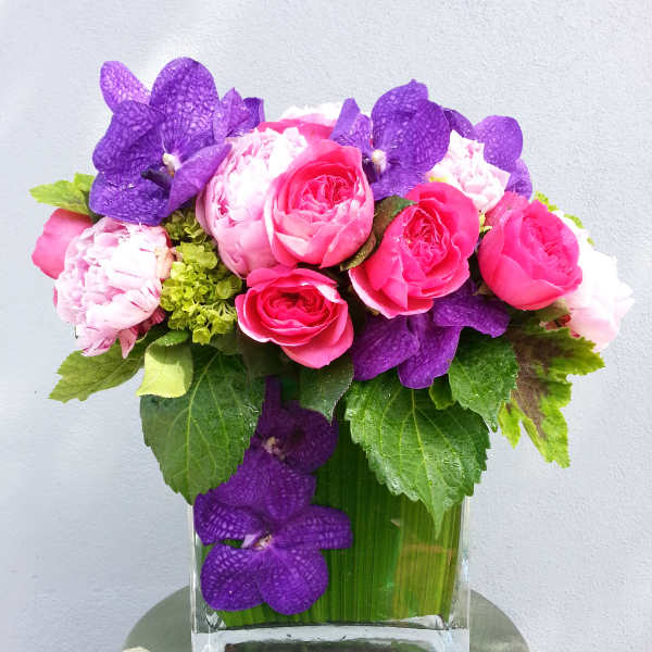 Pink roses and purple orchids arranged in a clear glass vase