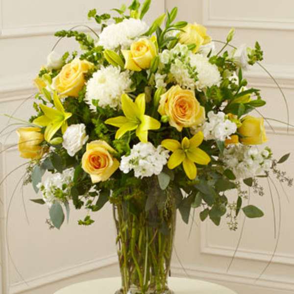 Yellow roses and white flowers arranged in a clear glass vase