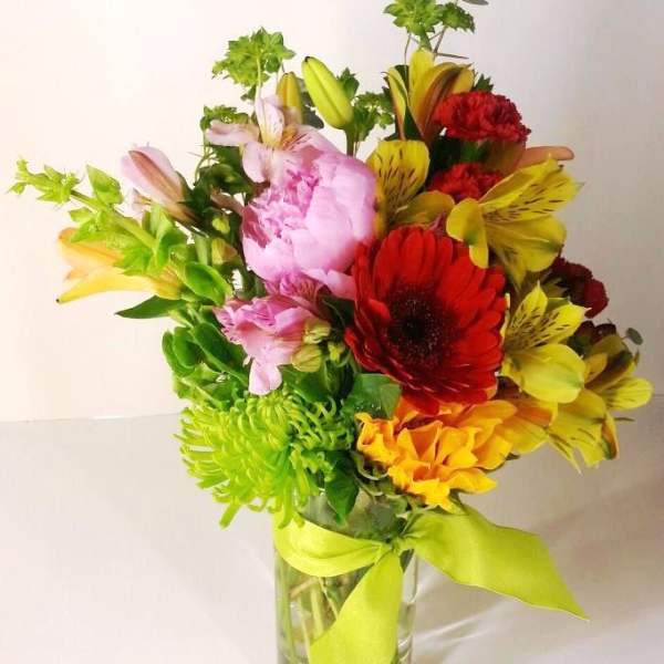 Colorful bouquet of mixed flowers in a clear glass vase with a lime ribbon