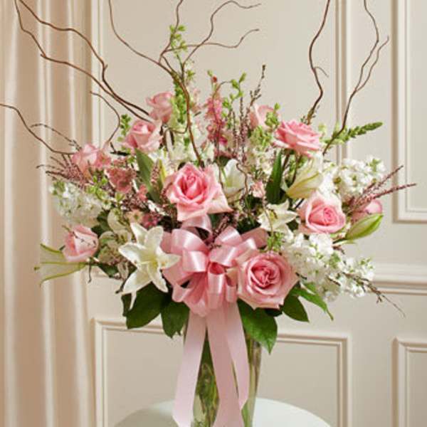 Pink roses and white lilies in a clear glass vase with a pink ribbon