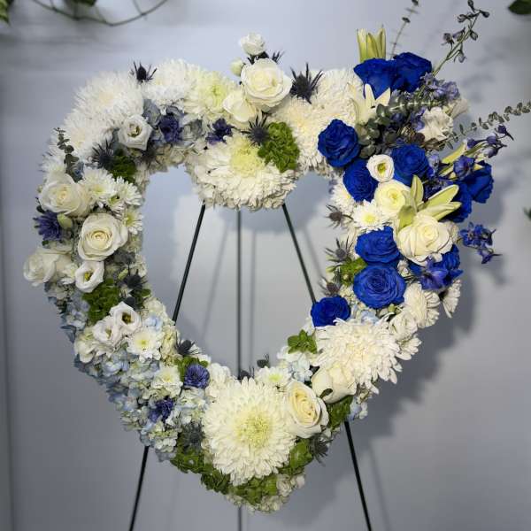 Heart-shaped floral wreath with white and blue flowers on a stand