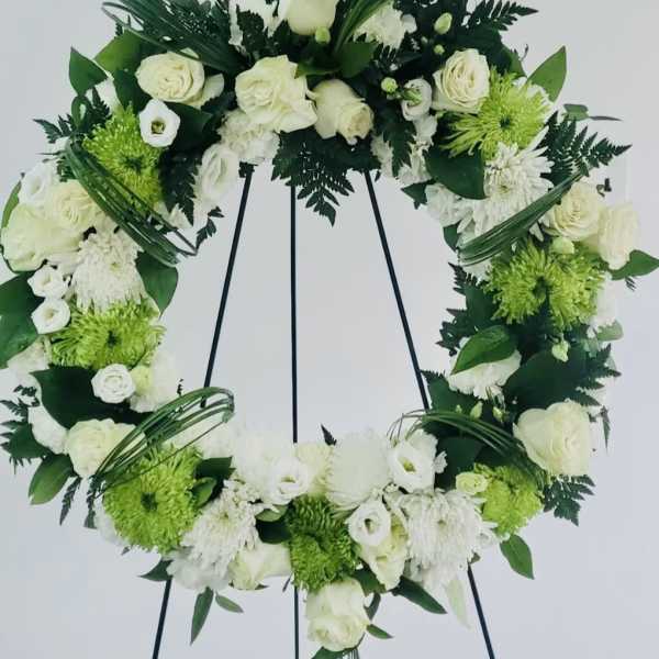 White floral wreath on a black stand with green accents