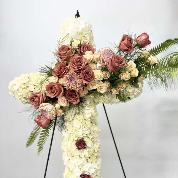 Cross-shaped floral spray with white hydrangeas and pink roses on a stand