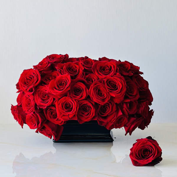 Red rose arrangement in a black rectangular vase with one loose rose beside it