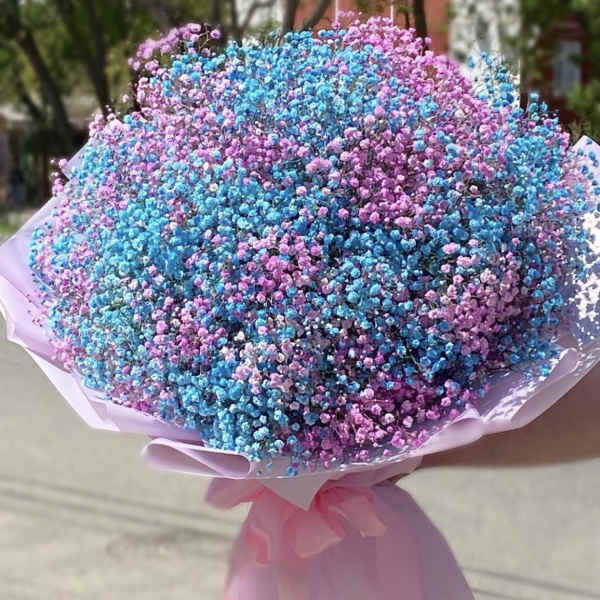 Large round bouquet of blue and pink tiny blooms wrapped in pale pink paper with a bow