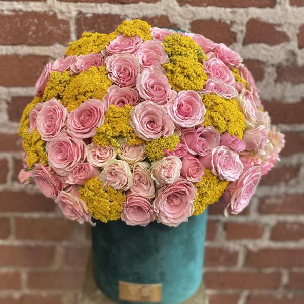 Round hatbox arrangement of pink roses and yellow filler blooms in a teal container