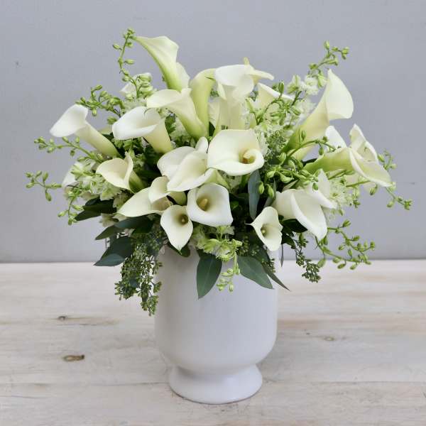 Arrangement of white calla lilies in a white pedestal vase