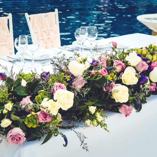 Long floral centerpiece with pink, white, and purple roses on a table by water