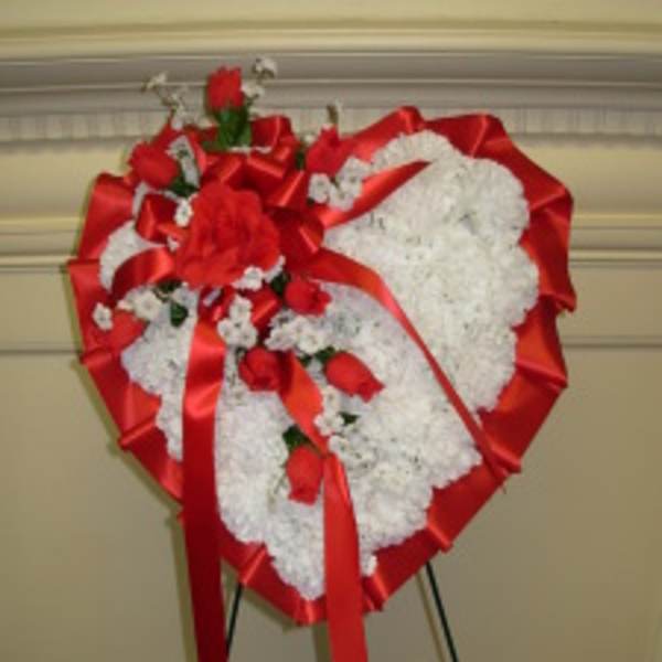 Heart-shaped white floral wreath with red roses and ribbon on an easel
