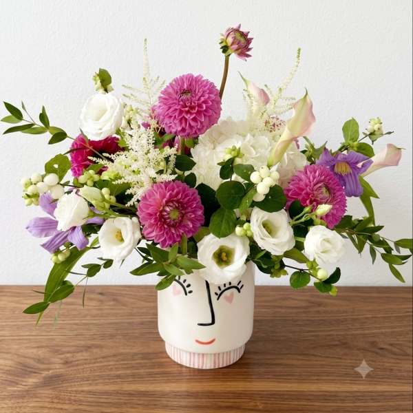 Mixed bouquet in a face-painted ceramic vase with pink, white, and purple blooms