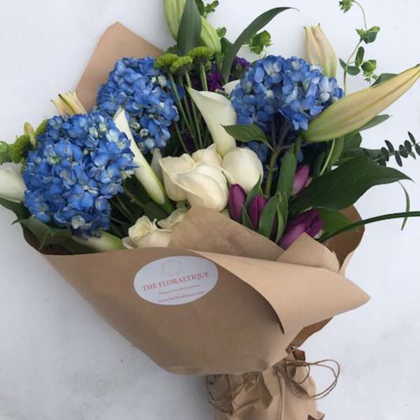 Bouquet of blue hydrangeas, white calla lilies, and purple tulips in brown paper