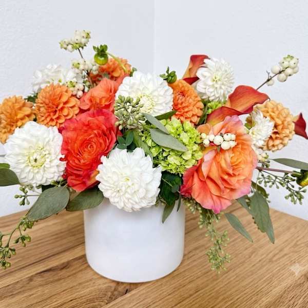 Mixed orange, white, and coral flowers arranged in a white vase