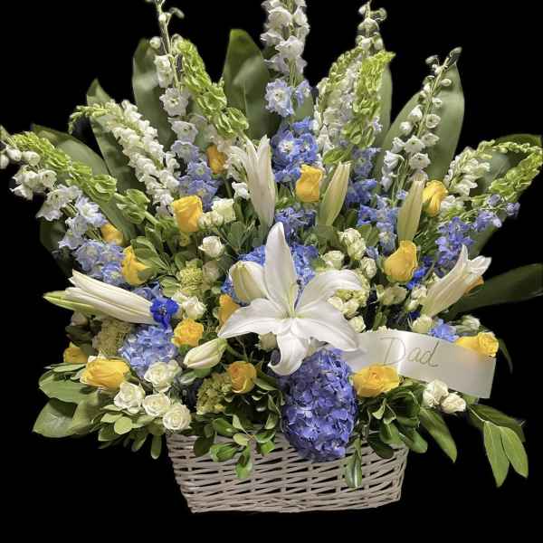 Basket arrangement of white lilies, yellow roses, and blue flowers with a Dad ribbon
