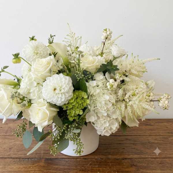 White floral arrangement in a white vase with roses, hydrangeas, and calla lilies