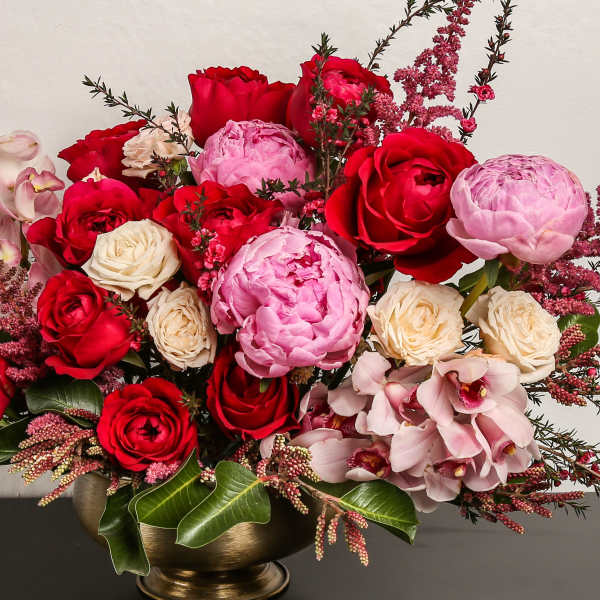 Bouquet of red and pink roses with pale orchids in a gold vase