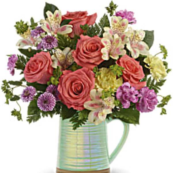 Bouquet of pink roses and mixed flowers in an iridescent pitcher vase