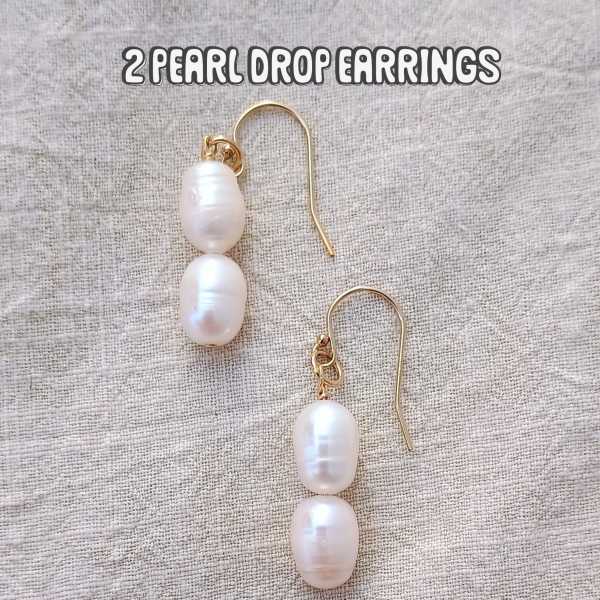 Pair of pearl drop earrings with gold hooks on a fabric background