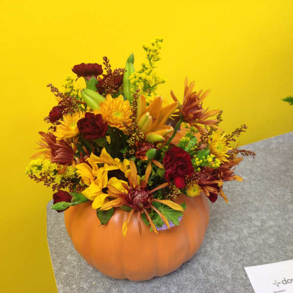 Autumn flower arrangement in a pumpkin container with yellow and burgundy blooms