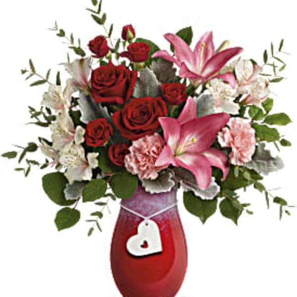 Red roses and pink lilies in a red vase with a heart charm