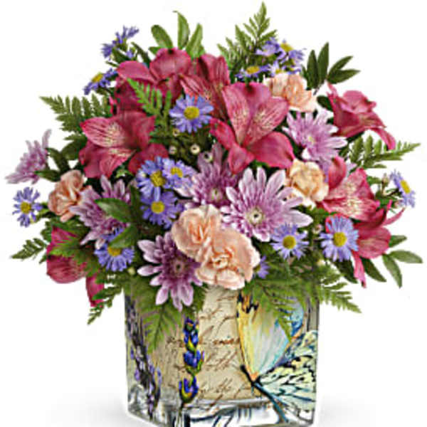 Mixed bouquet of pink, purple, and peach flowers in a decorative square vase